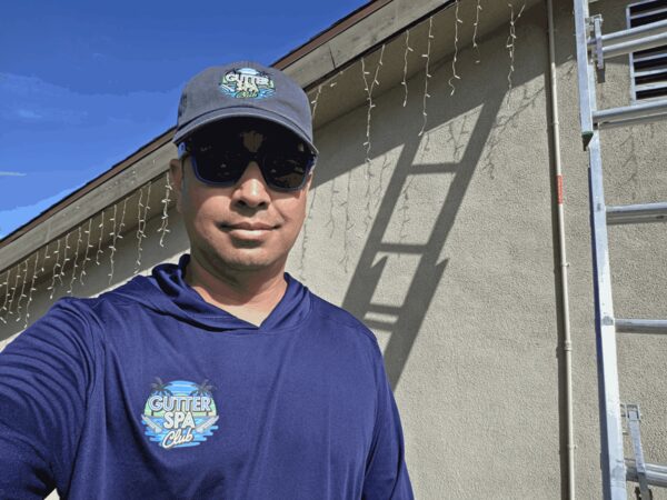Ritchie, owner of Gutter Spa Club, in a company hat and shirt next to a ladder on a job